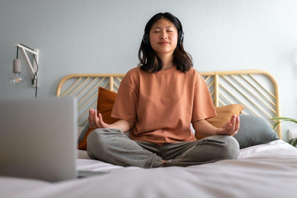 teen girl meditates sitting on bed following personalized recording from Mind Over Everything, listening with headphones.
